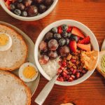 A fresh and vibrant breakfast flat lay featuring a yogurt bowl with fruits and toast with eggs and avocado.